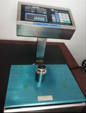 Báscula digital con pesa metálica sobre su plataforma azul, que muestra una lectura de 10000.