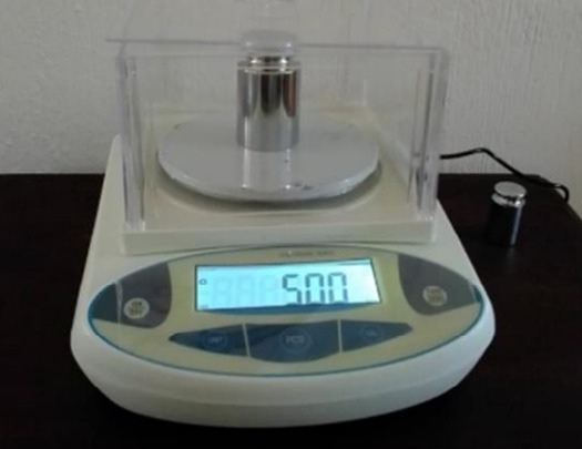 Báscula digital que muestra una lectura de 5,00 con un peso cilíndrico en la plataforma.