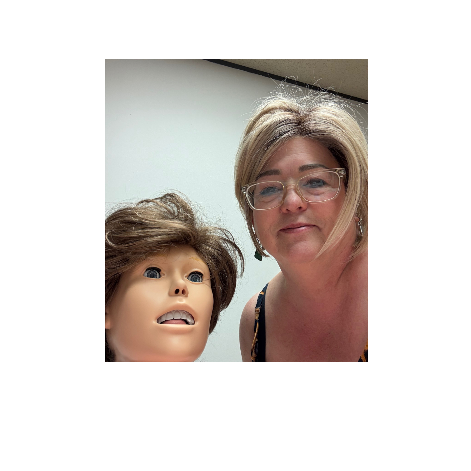 Woman with glasses smiles next to a mannequin head with teeth and hair.