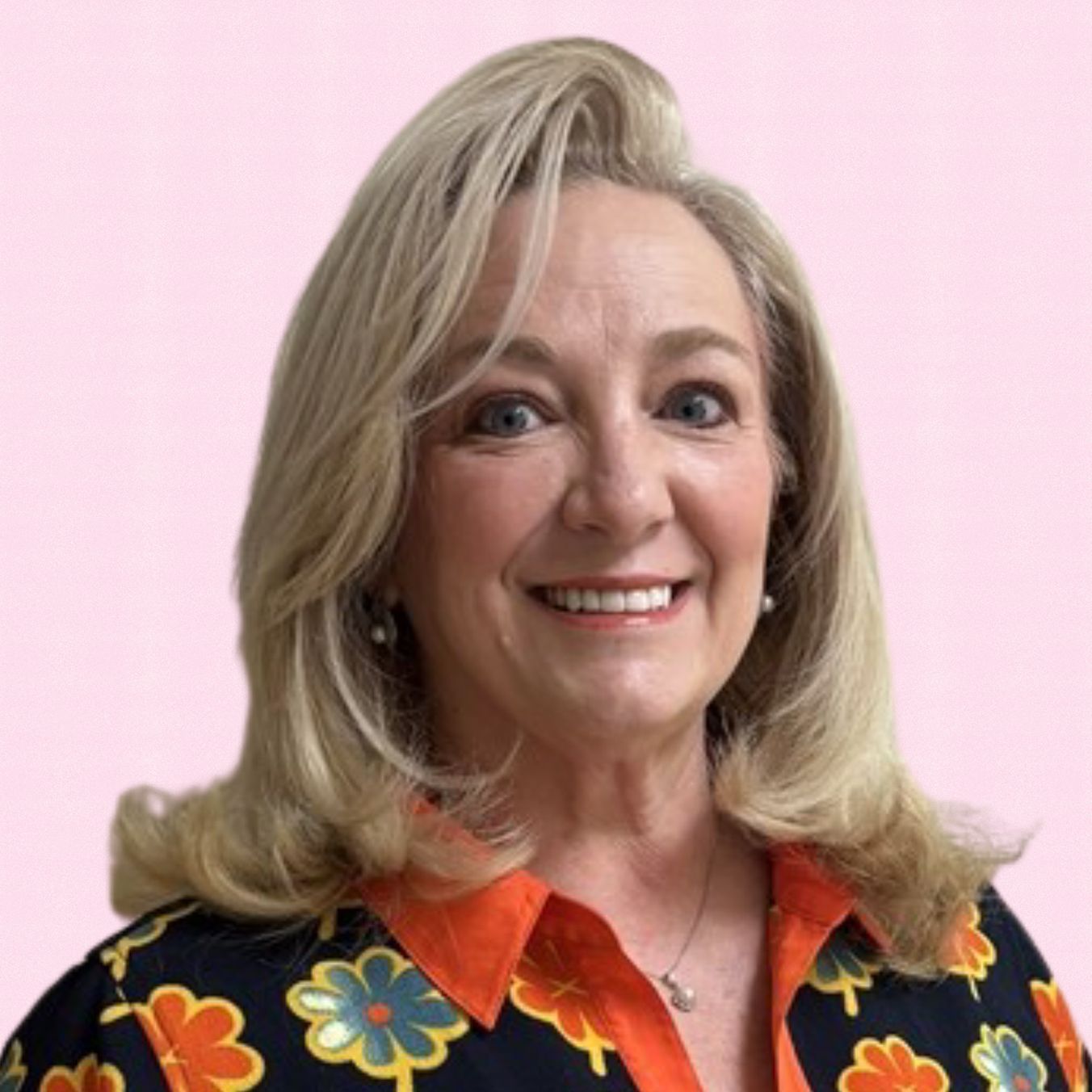 Woman with blonde hair smiles, wearing a colorful floral shirt against a pink background.