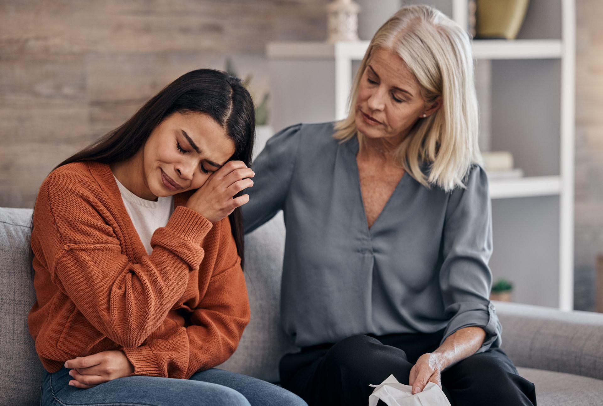 A woman is comforting a woman who is crying while sitting on a couch.