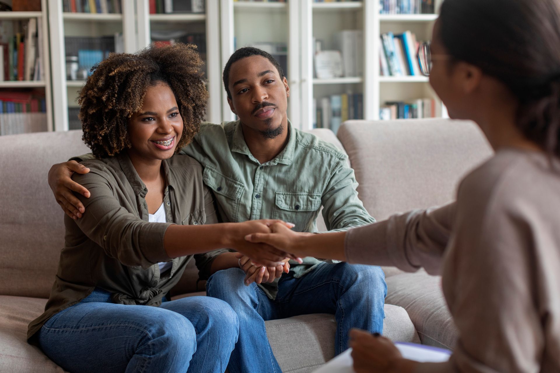 A man and woman are sitting on a couch shaking hands with a woman.