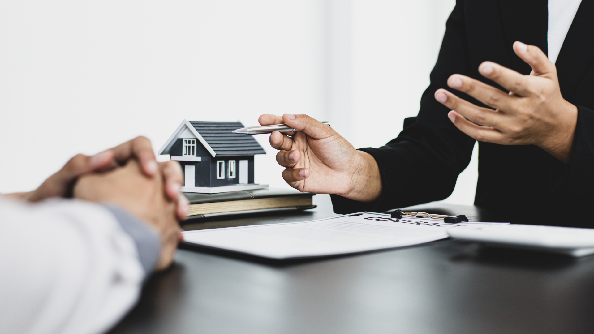 A man and a woman are shaking hands in front of a model house.