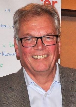 Ein Mann mit Brille und Anzug lächelt in die Kamera.