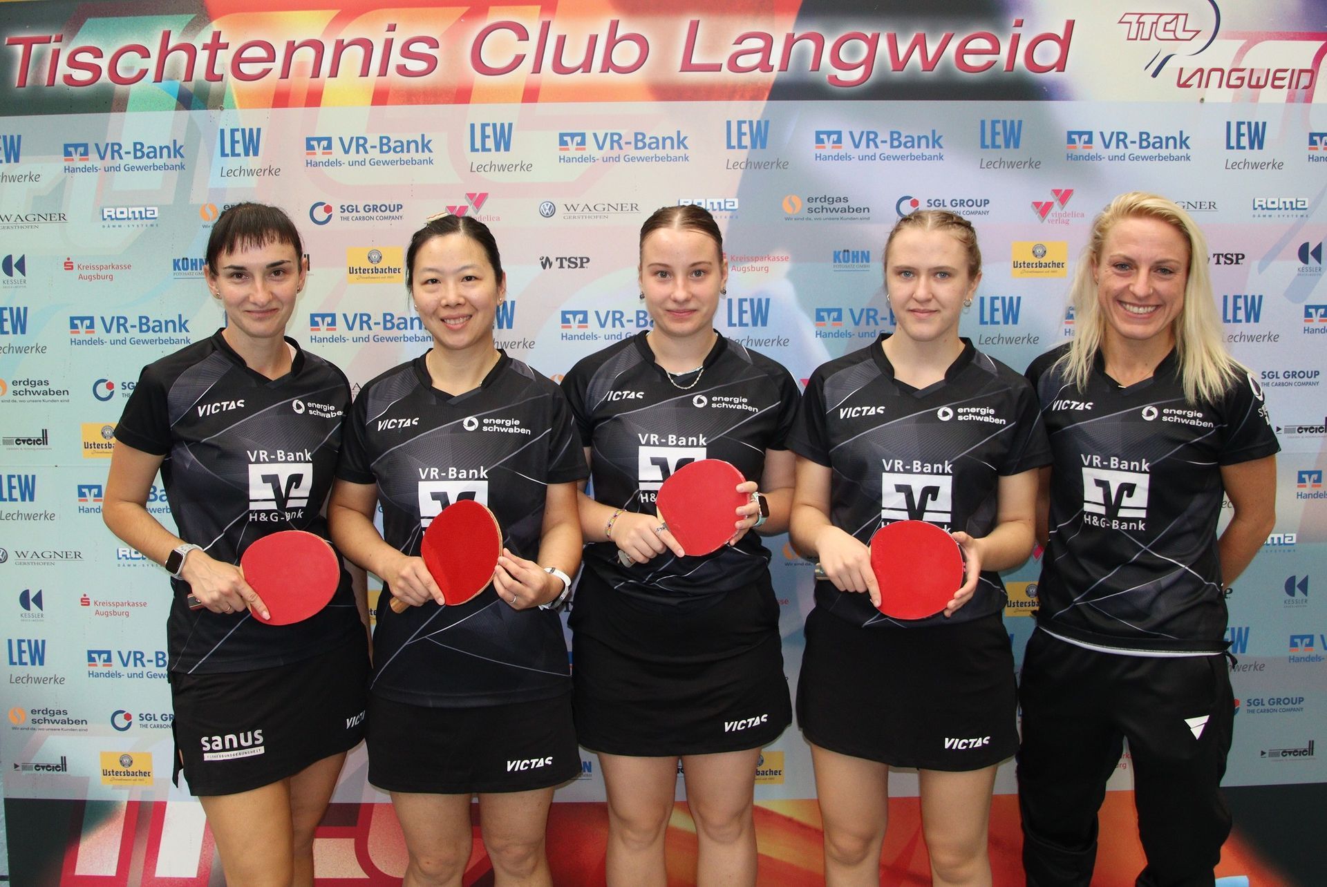 Eine Gruppe von Frauen mit Tischtennisschlägern vor einem Schild mit der Aufschrift „Tischtennis Club Langweid“