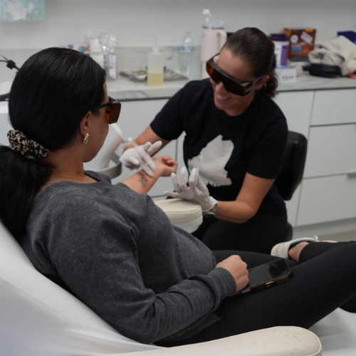 A person receiving laser treatment on their hand in a clinic. Another person is operating the laser.