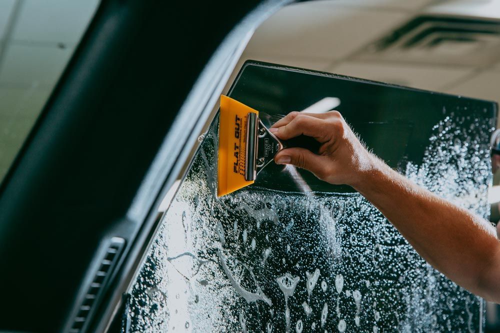 A person is applying tinted window film to a car window.