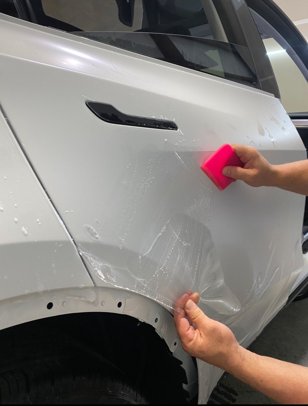 A person is applying a protective film to the side of a white car.