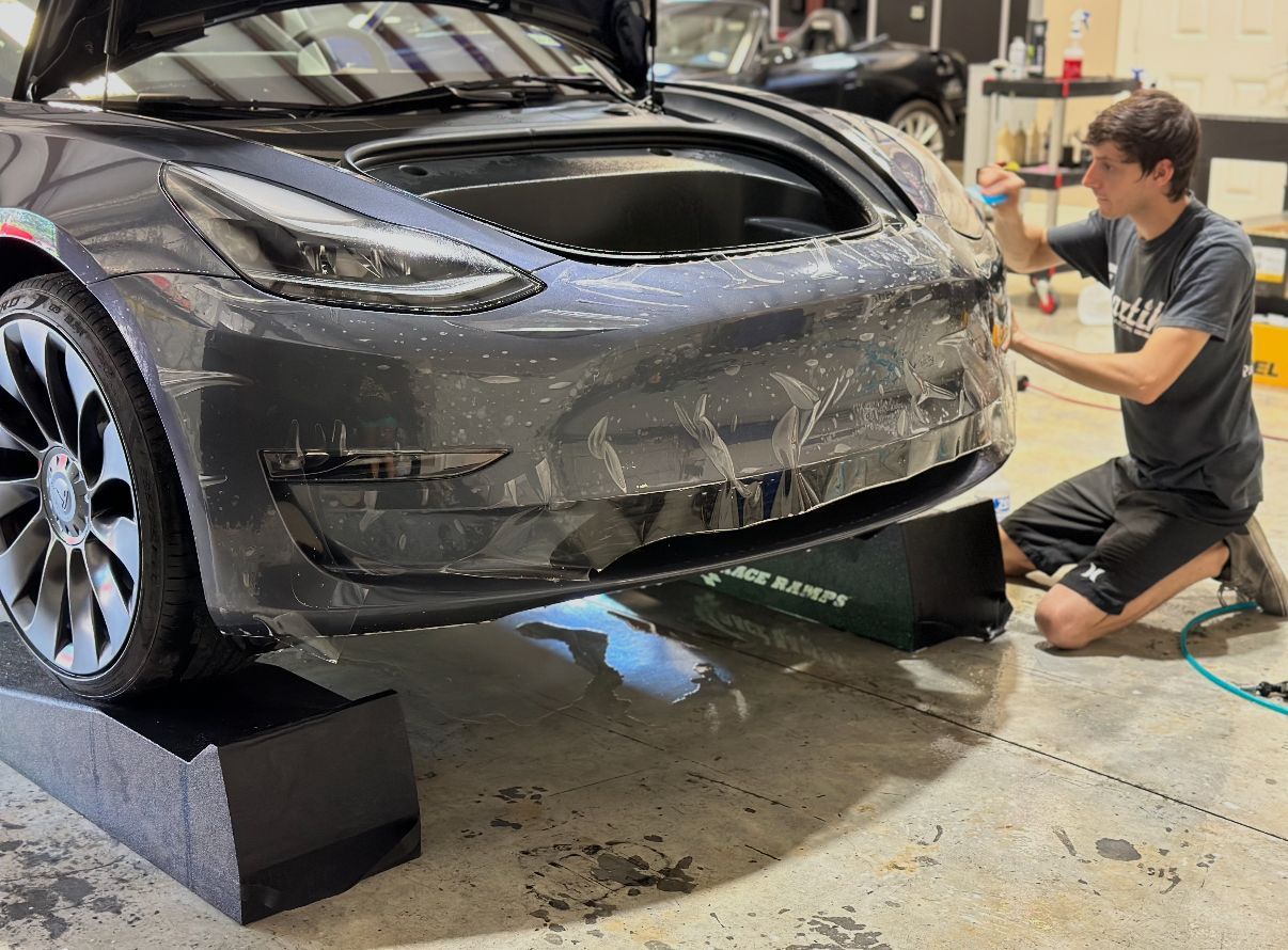 A man is kneeling down in front of a tesla model 3.