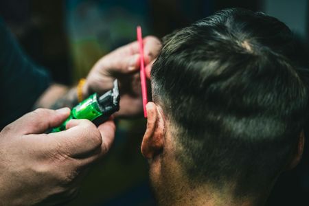 Barber trimming the back of a client’s hair with clippers and a red comb