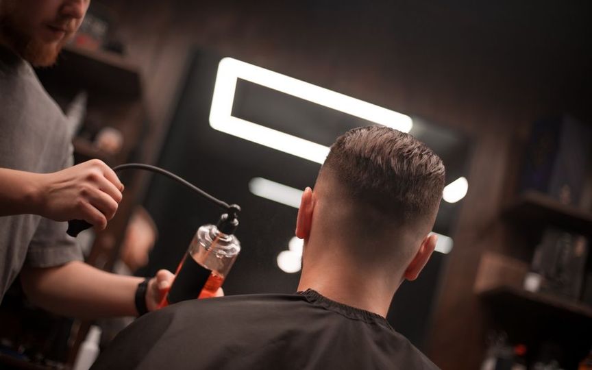 A barber applies spray to a customer’s hair in a dimly lit salon, focusing on a fresh haircut.