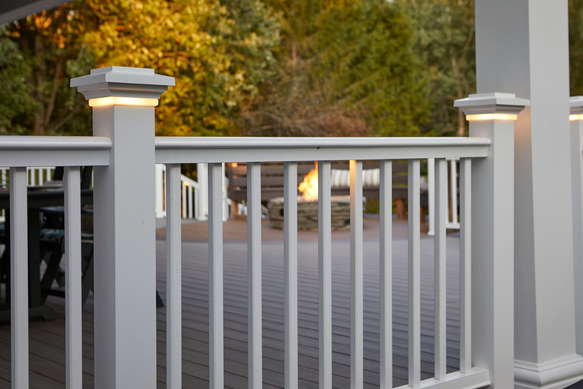 A white railing on a deck with a fire pit in the background.