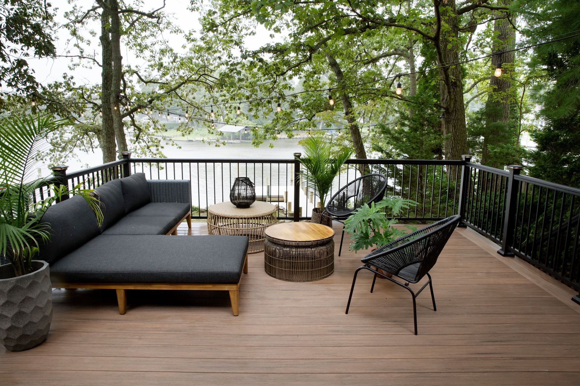 A deck with a couch , chairs and a fire pit overlooking a lake.