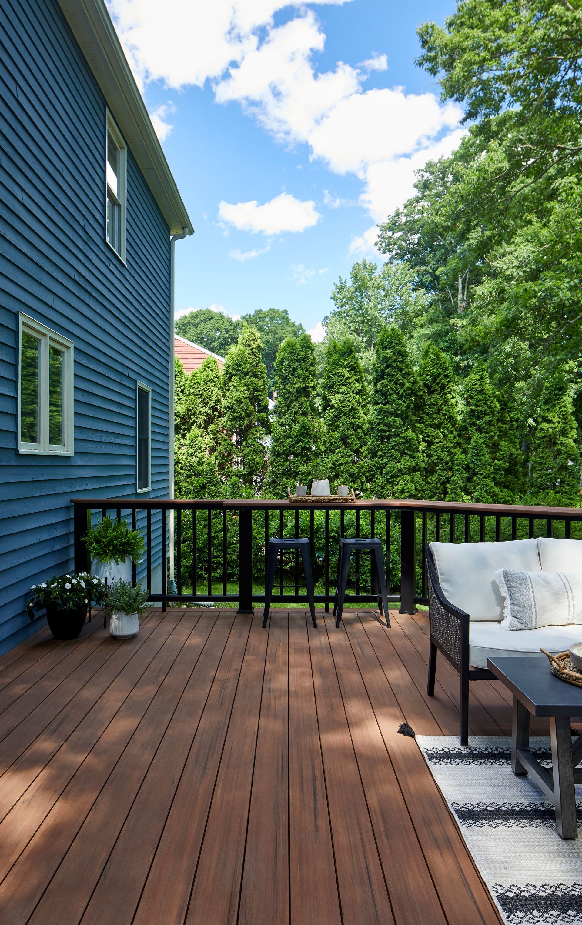A wooden deck with a couch , table and chairs in front of a blue house.