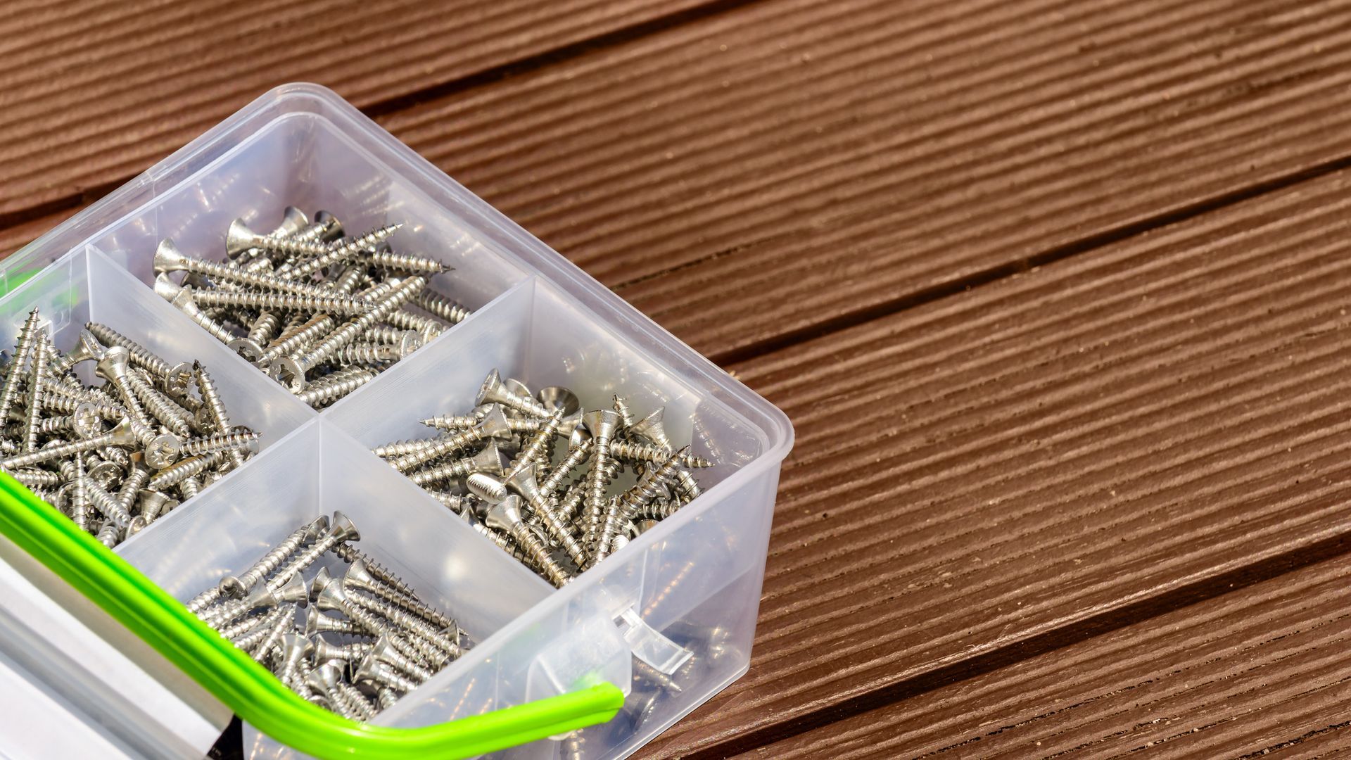 A plastic box filled with screws is sitting on a wooden table.
