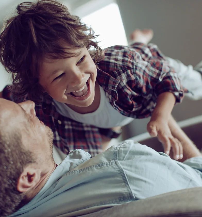 A little boy is laying on top of a man on a couch.