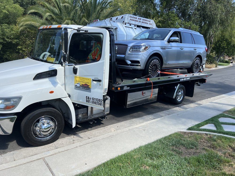 Silver SUV on a flatbed tow truck on a suburban street, green grass in the foreground.