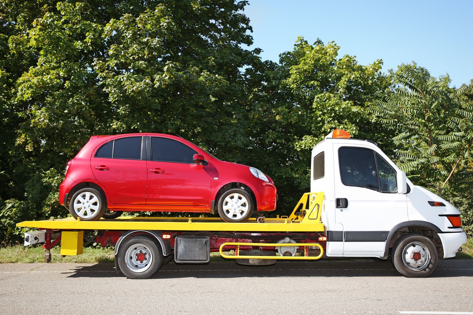 Red car being transported on a white tow truck with a yellow flatbed.