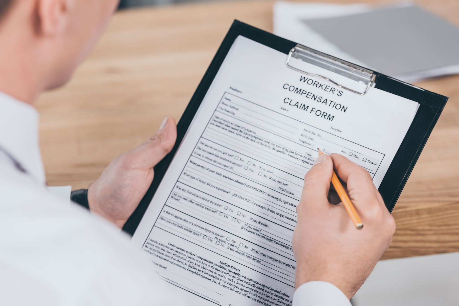 Person filling out a worker's compensation claim form on a clipboard with a pencil.