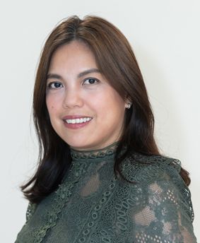 Woman with brown hair smiles, wearing a green lace top, against a white background.