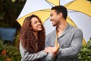 Smiling couple under a yellow and white umbrella, outdoors in a garden setting.