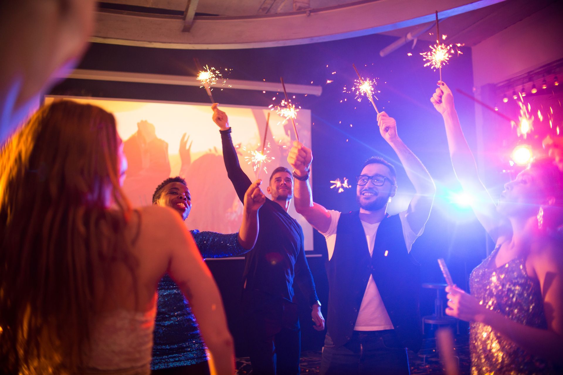 People celebrating in a club with sparklers, lit with colorful lights.