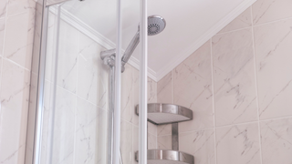 A shower stall with a shower head and a shelf in a bathroom.