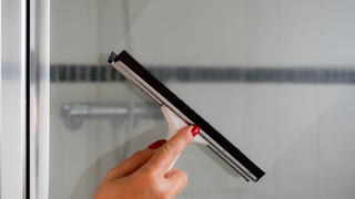 A woman is cleaning a shower door with a squeegee.