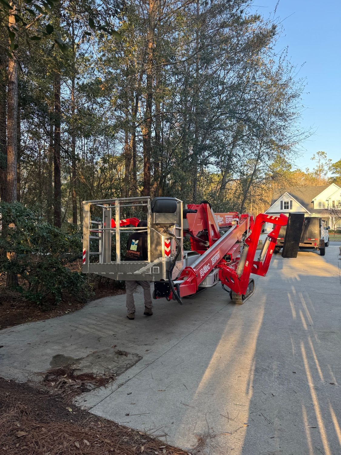 Large red cherry picker parked on a driveway beside a wooded residential street
