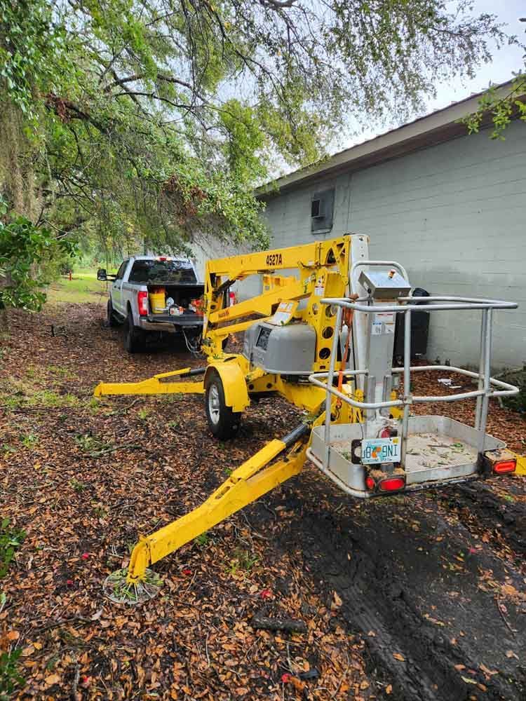 Yellow lift trailer parked near a house and truck, set up on uneven ground.