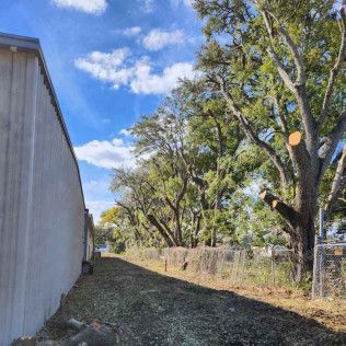 A gravel path next to a building, fence, and trees under a cloudy sky.