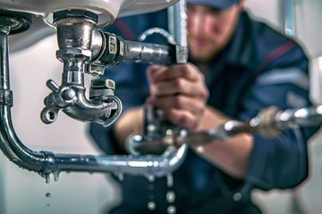 Plumber fixing leaky pipes under a sink. Water drips.