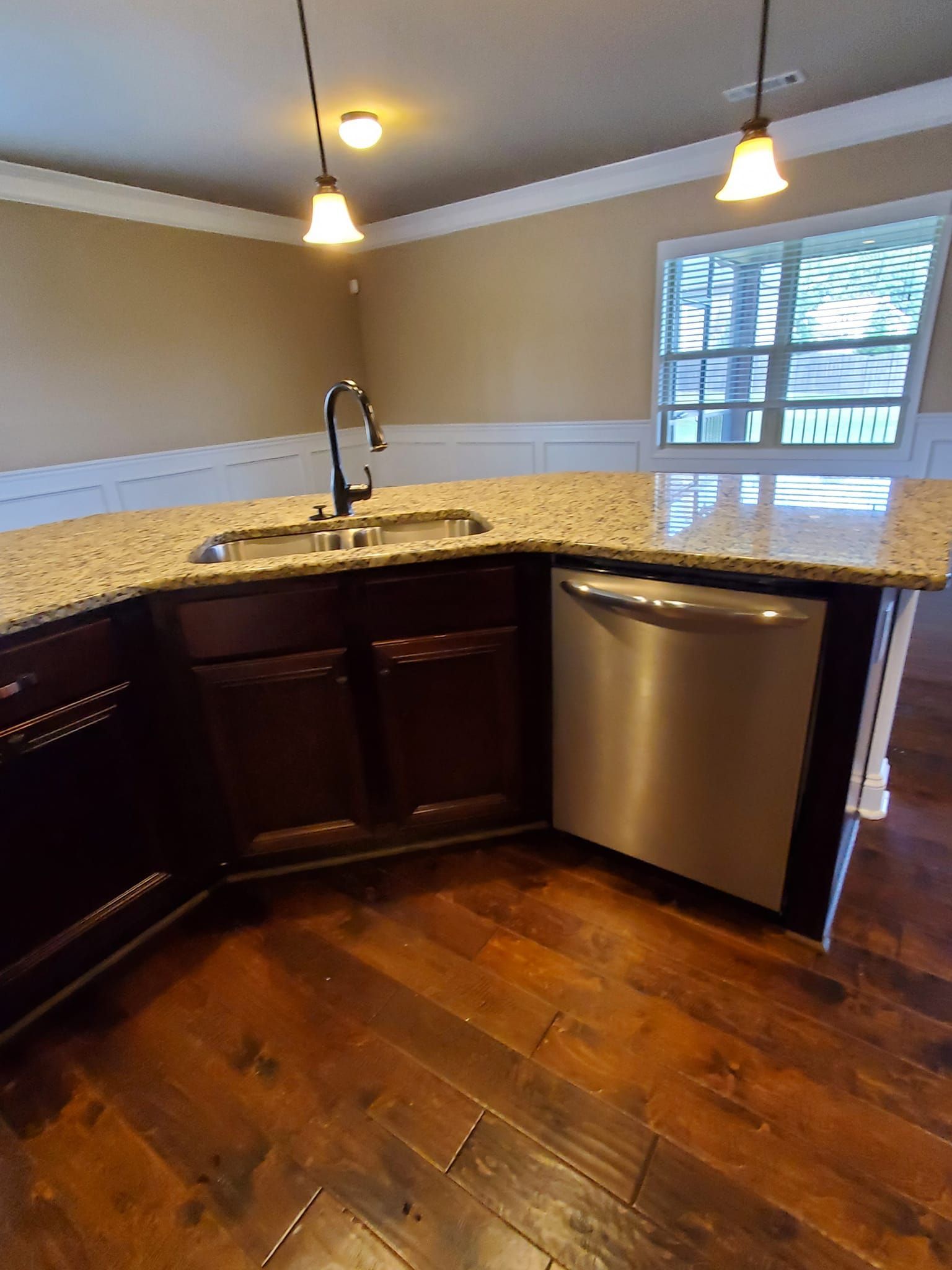 Kitchen island with granite countertop, dark cabinets, and a stainless steel dishwasher.