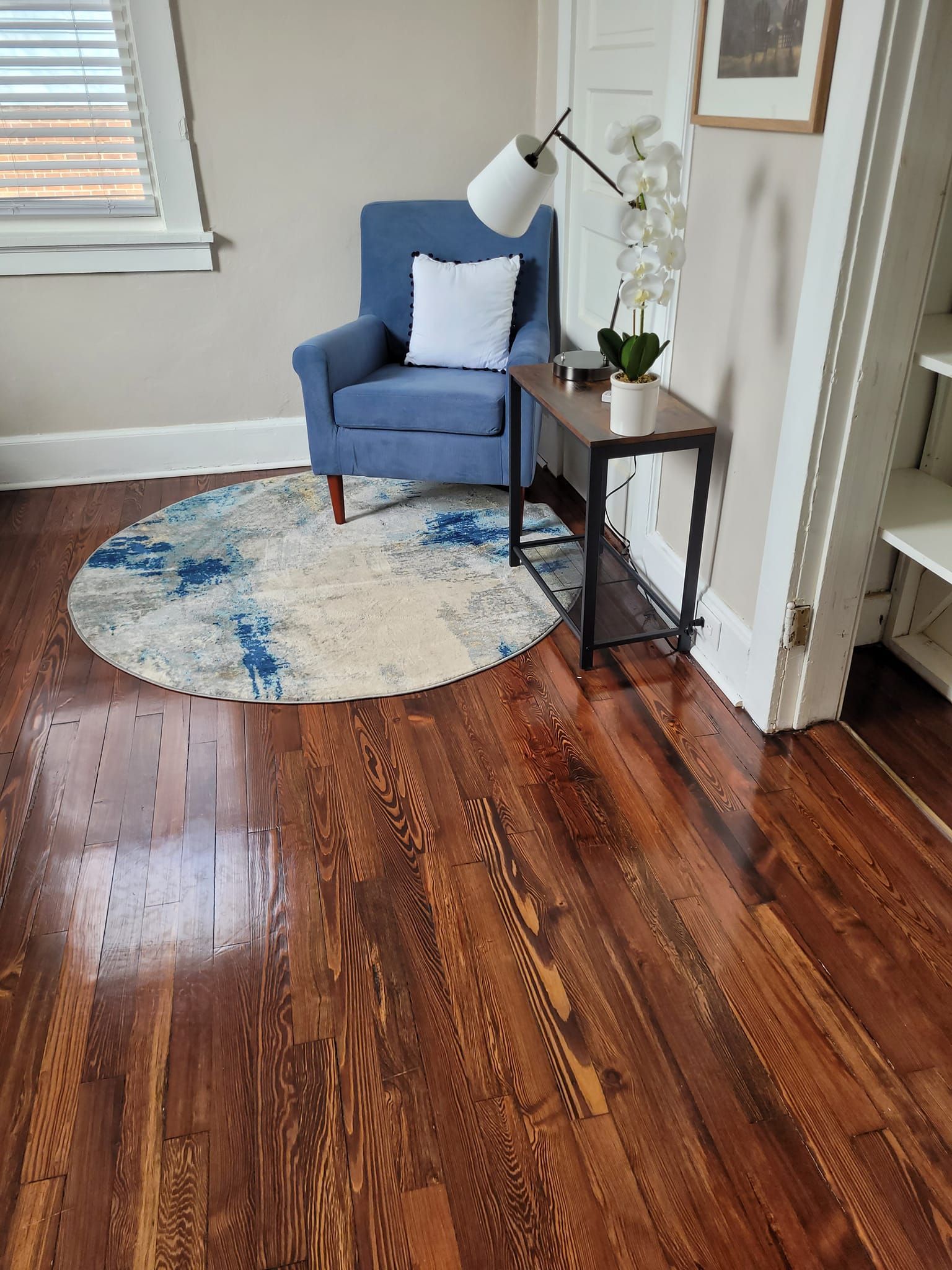 Blue armchair with white pillow, small table, and round rug on wood floor.