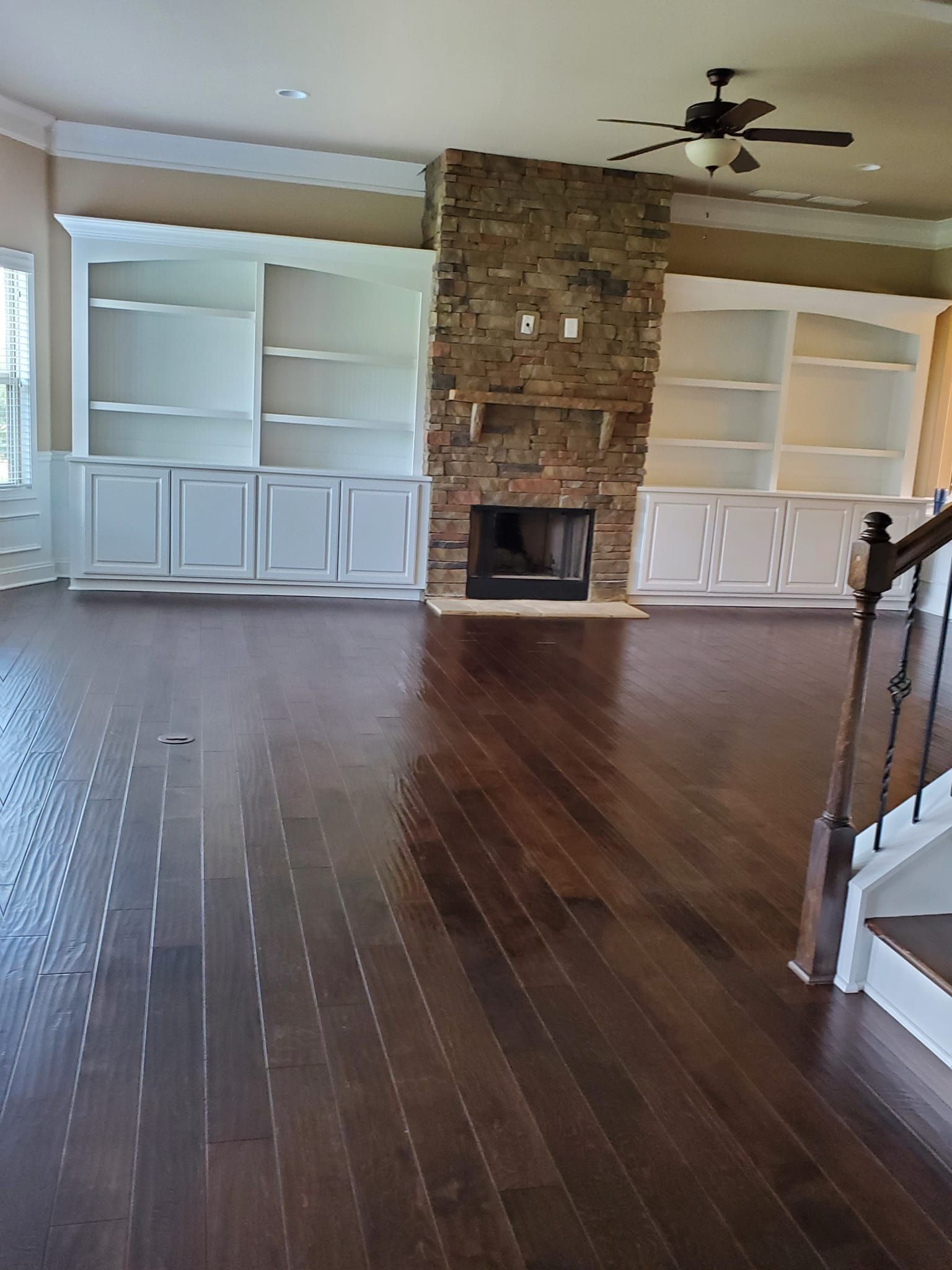 Living room with dark wood floors, stone fireplace, and white built-in bookshelves.