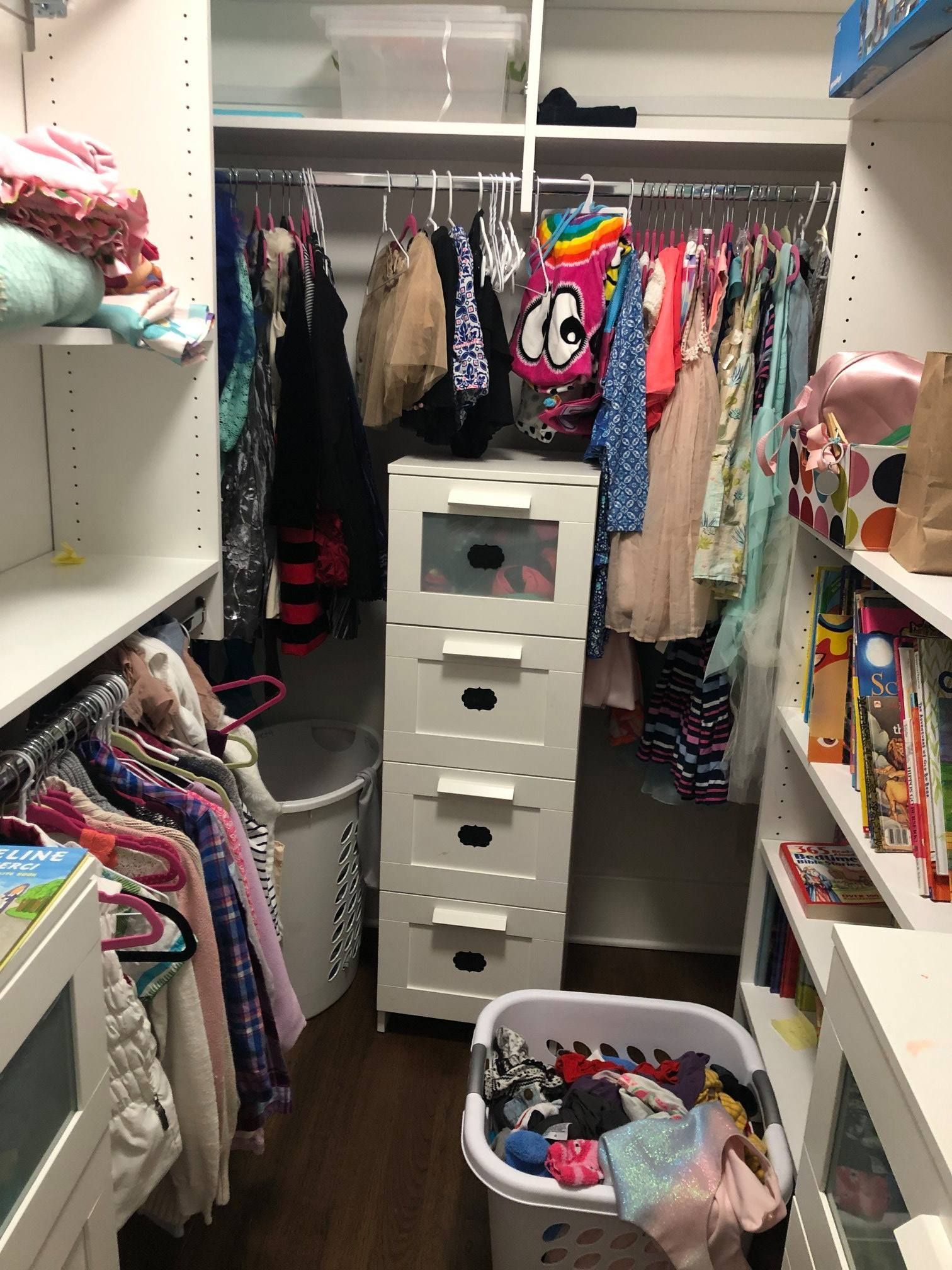 Walk-in closet with clothes hanging, shelves with items, and a white dresser.