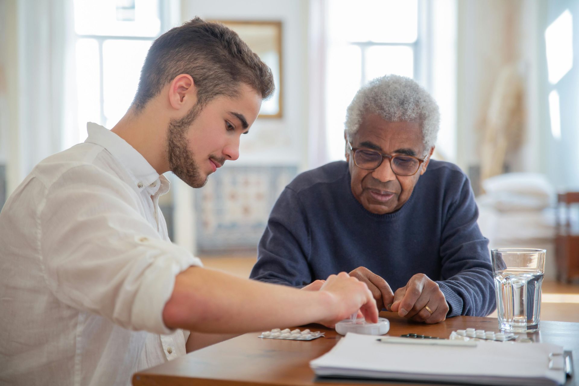 A young man is helping an older man with his medication.