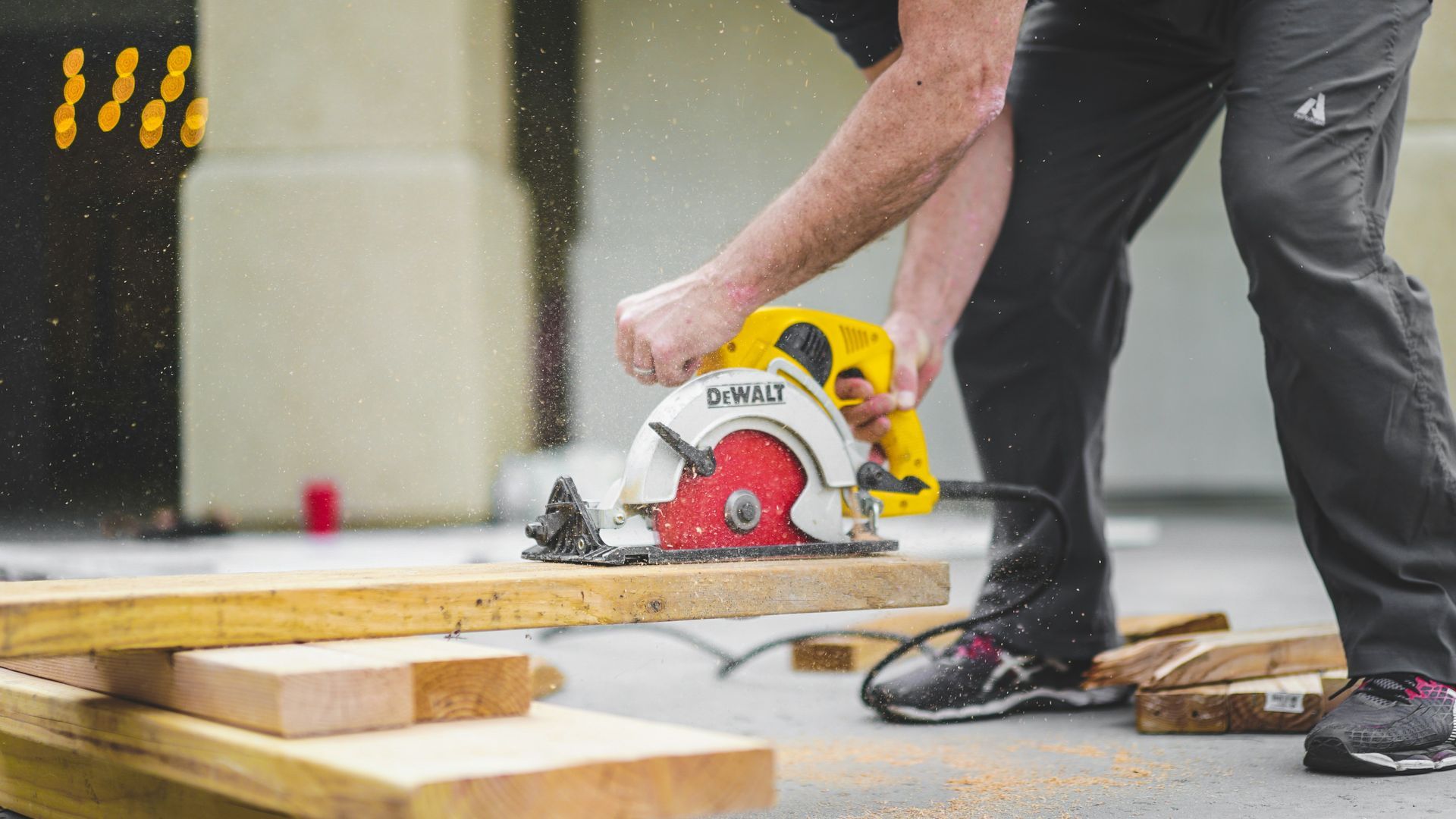 Worker using a red circular saw to cut a wooden plank on a construction site
