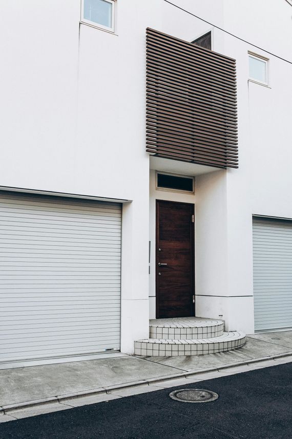White building facade with a dark wooden door, frosted garage-style panels, and a large textured balcony screen.