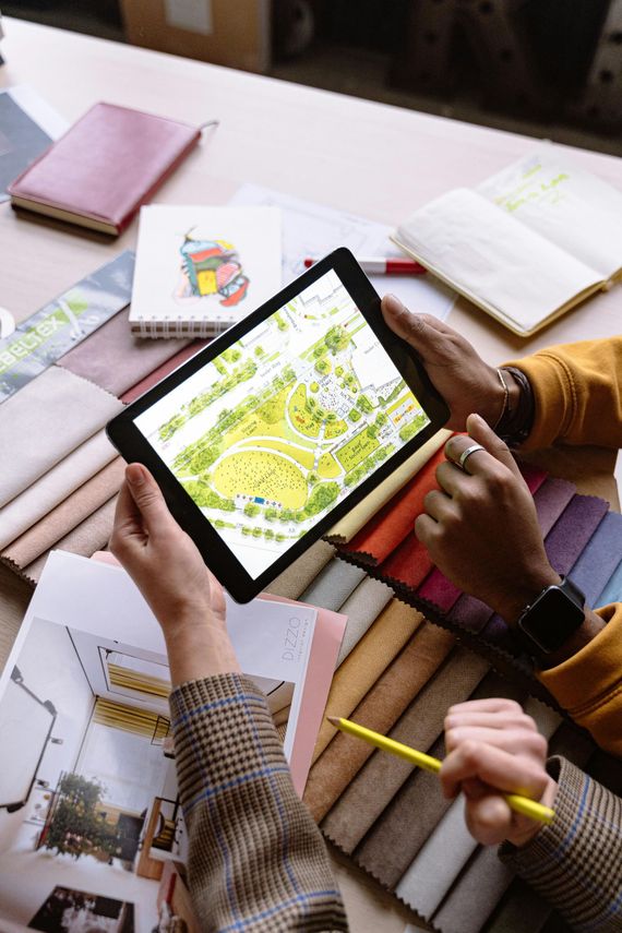 People using a tablet to view a colorful map at a desk with notebooks and pencils