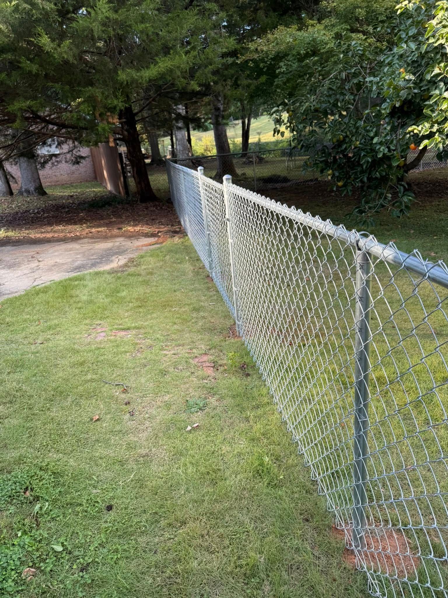 A chain link fence along a sidewalk in a park.