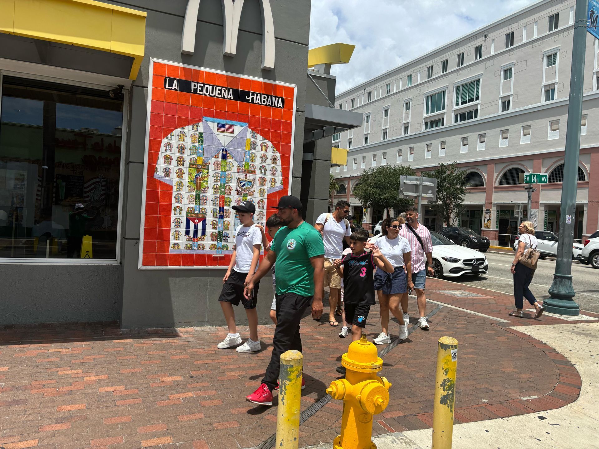 Families exploring Calle Ocho during a cultural stop on the Miami City Bus Tour, in front of the iconic La Pequeña Habana mural.