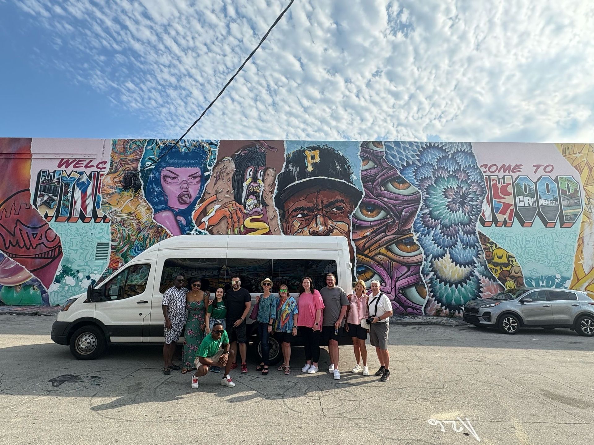 Group of passengers posing in front of the Miami Tour Bus at Wynwood Walls
