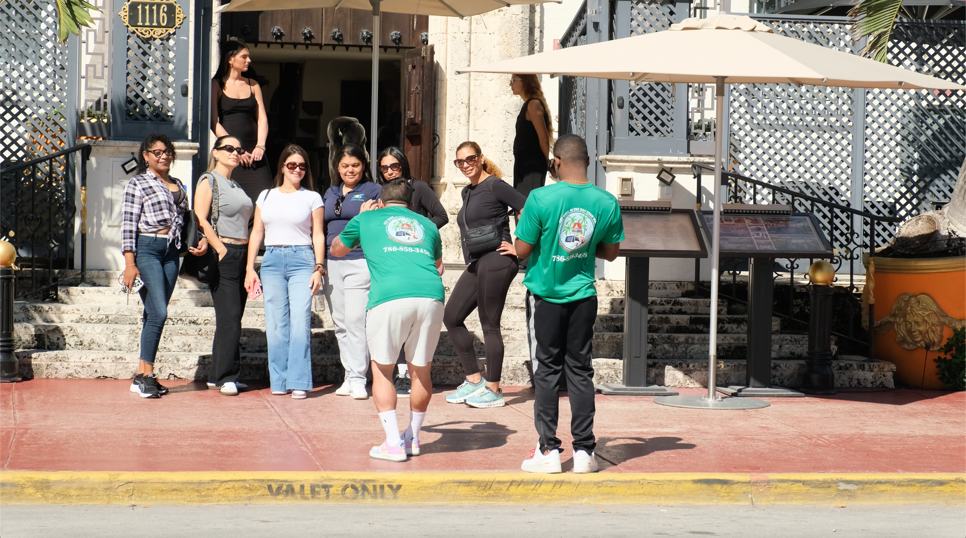 Group of happy tourists with Miami Tour Bus guides posing in front of the Versace Mansion on Ocean Drive, Miami.
