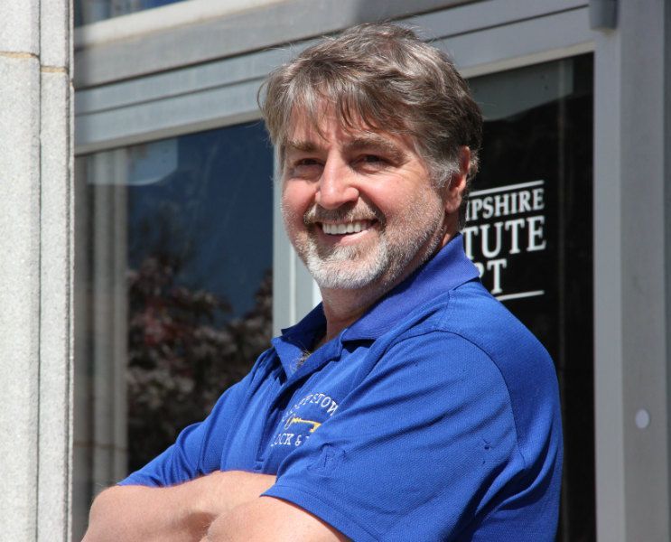 A man in a blue shirt stands in front of a sign that says tipshire tute