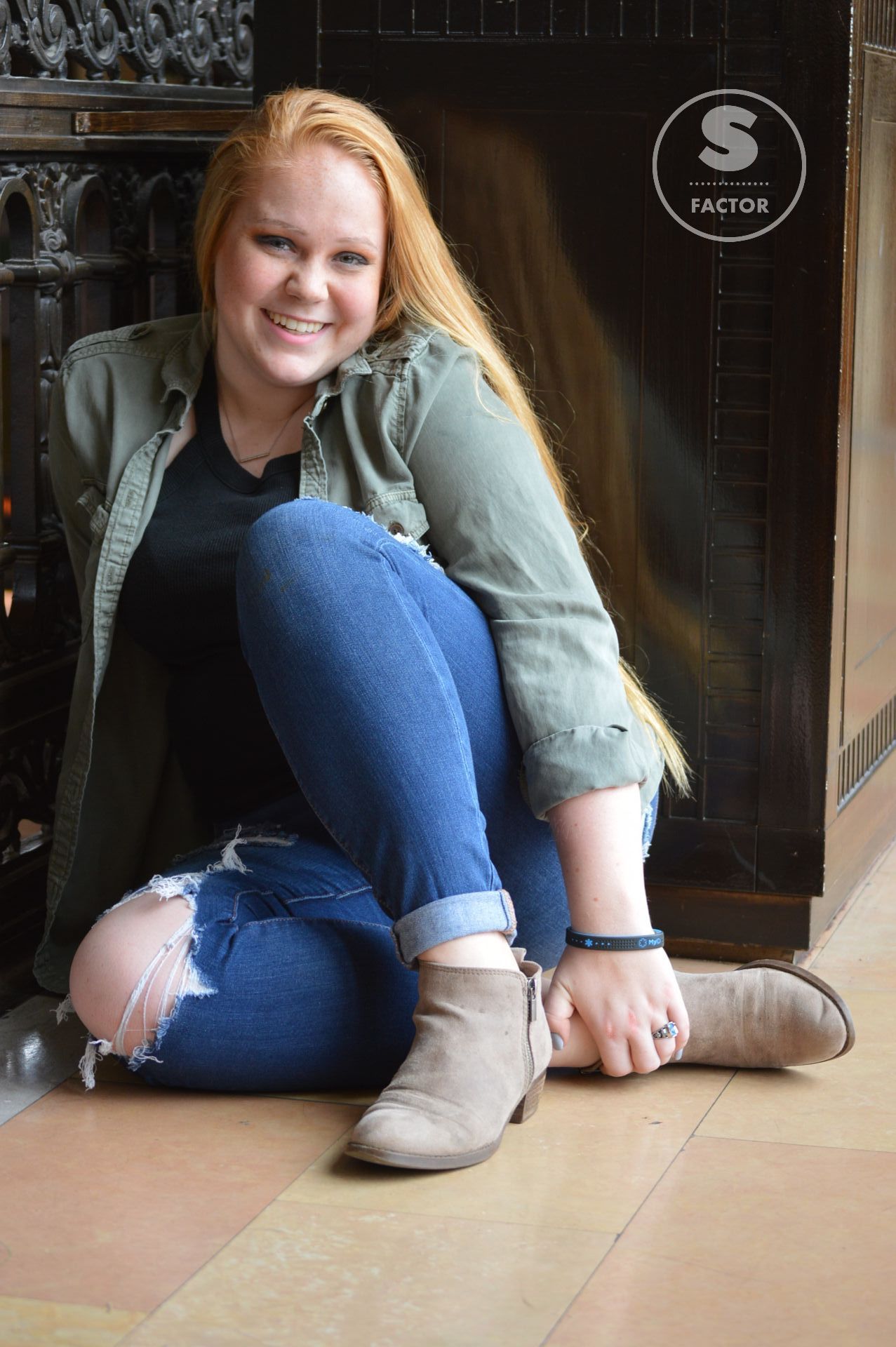 A woman is sitting on the floor with her legs crossed and smiling.