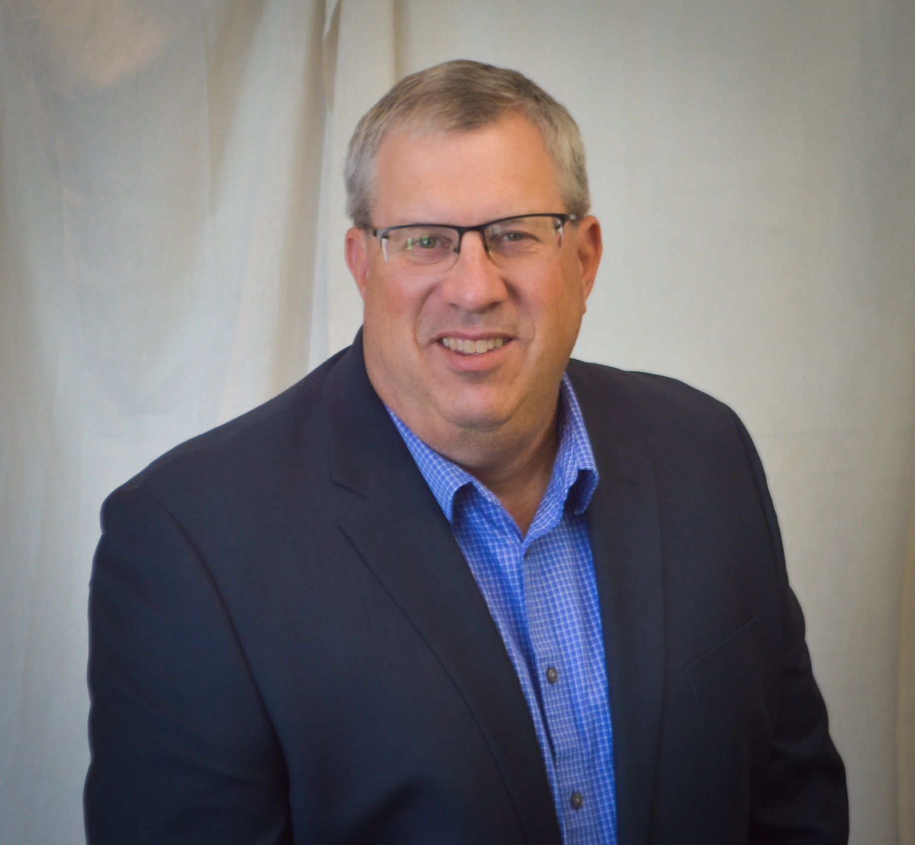 A man in a suit and glasses is smiling for the camera