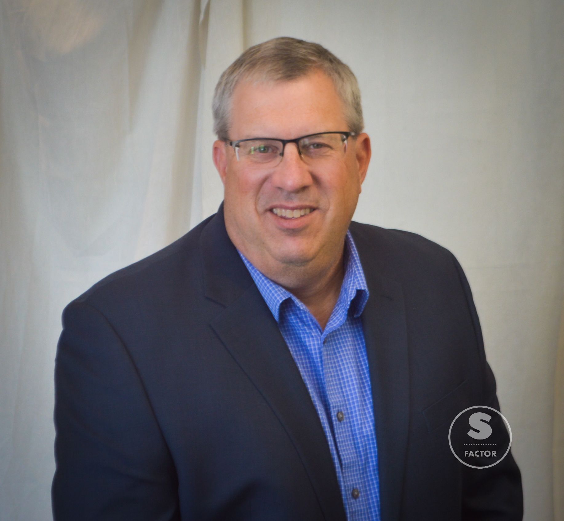 A man wearing glasses and a suit is smiling for the camera