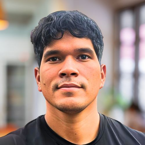 Man with dark hair and a neutral expression, wearing a black shirt, indoors with a blurred background.