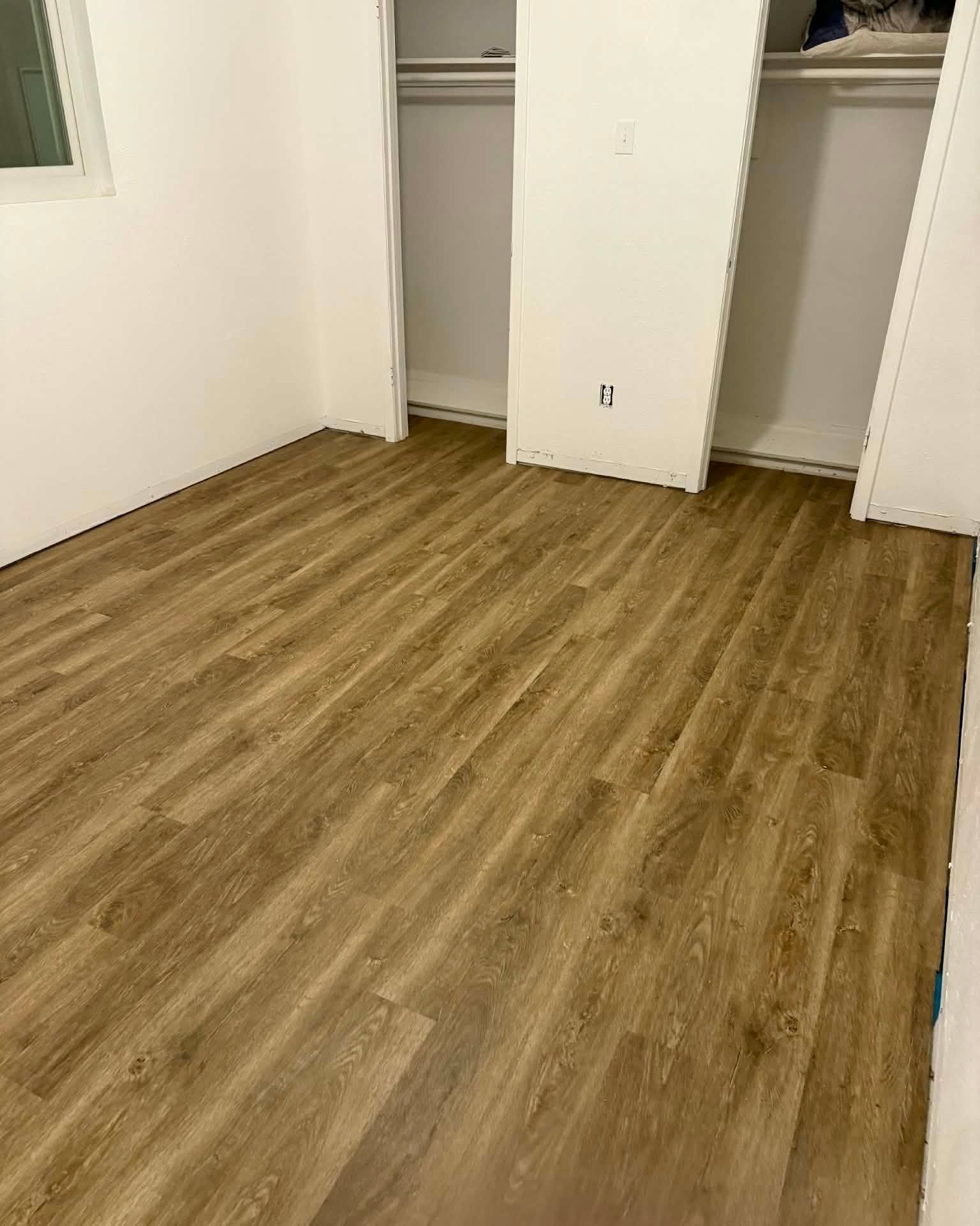Empty room with wood-look flooring and open closet doors against white walls.